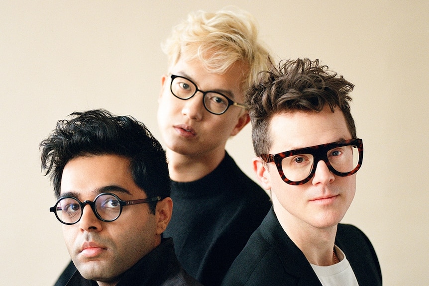 The three members of Son Lux wearing glases and looking to the camera against a cream background