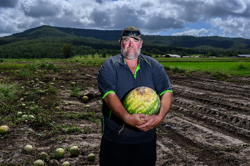 Man standing in a paddock holding a watermelon