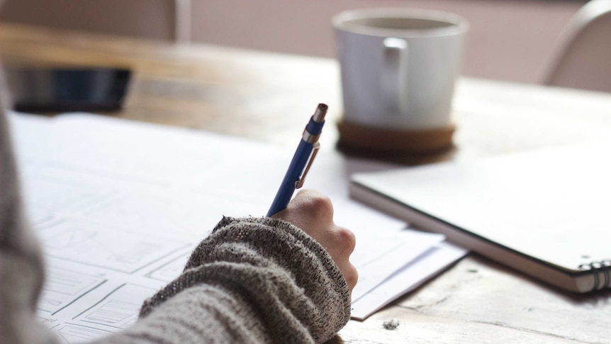 Close up of hand writing on paper with a coffee cup behind