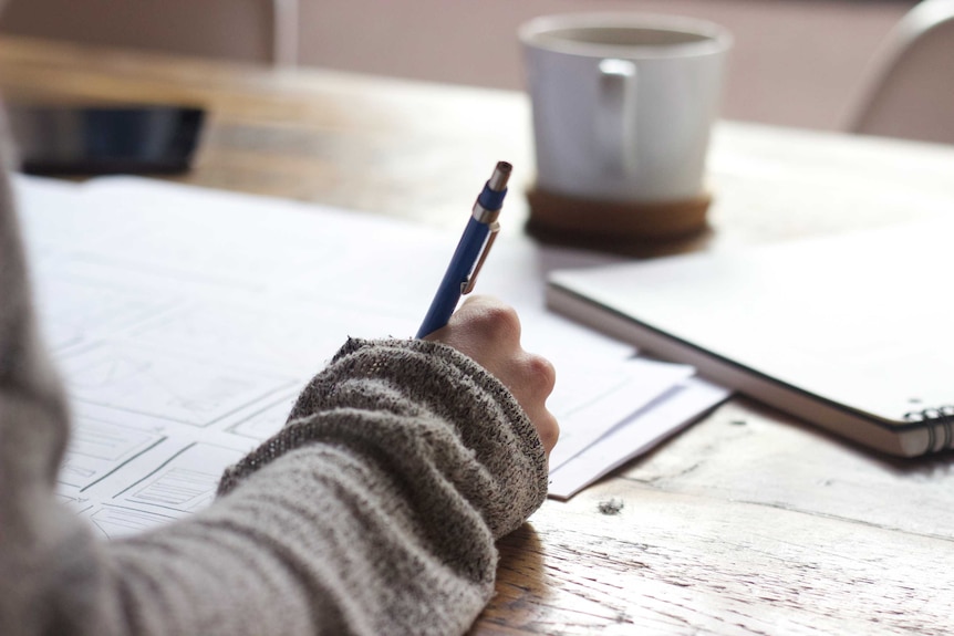 Close up of hand writing on paper with a coffee cup behind