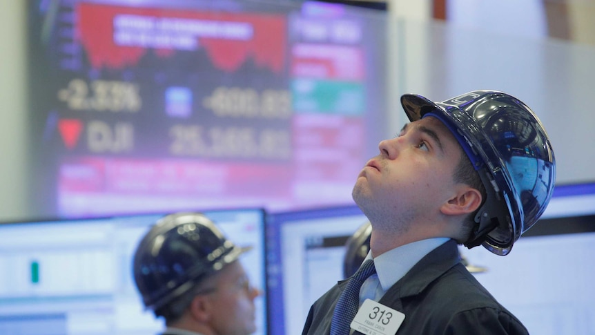 A trader, wearing a blue helmet, looks up at the screen at the New York Stock Exchange