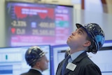 A trader, wearing a blue helmet, looks up at the screen at the New York Stock Exchange