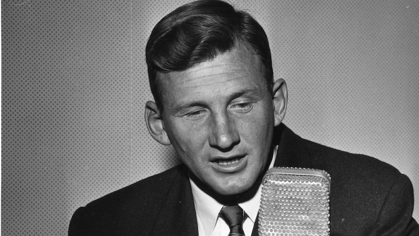 A black and white photo of Norman May speaking into the microphone.