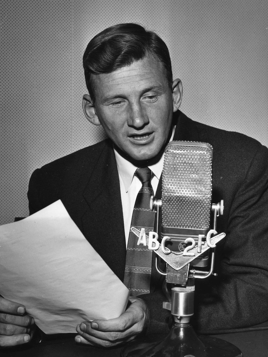 A black and white photo of Norman May speaking into the microphone.