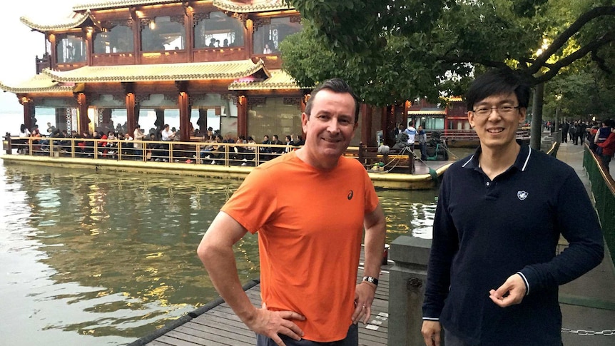 Two men standing in fr0ont of a pagoda-style floating restaurant.