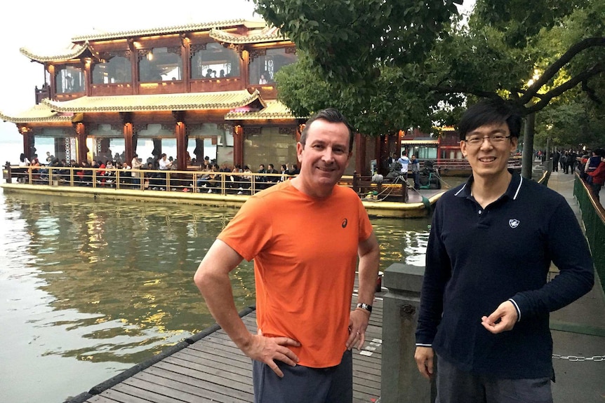 Two men standing in fr0ont of a pagoda-style floating restaurant.