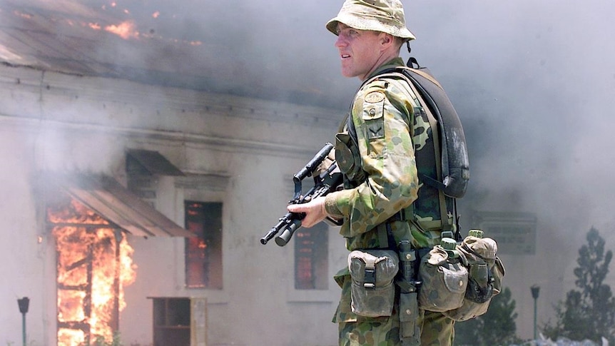 A soldier with a gun standing in front of a burning building