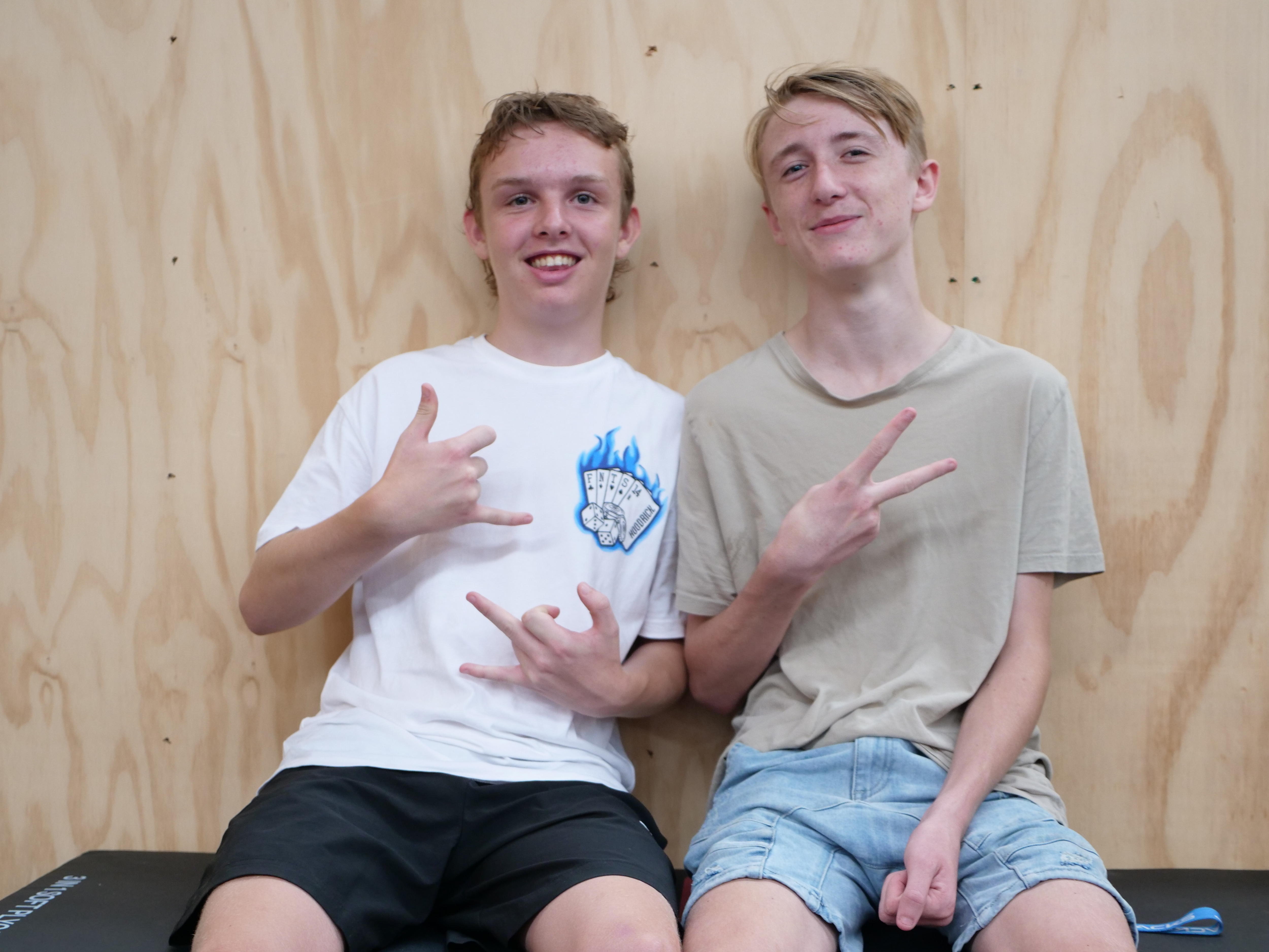 Two teen age boys sit together doing gang signs smiling 