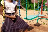 A girl sits on a swing. Her face cannot be seen in the photo. 