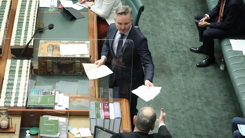 Bowen stands at the despatch box of the lower house while passing a sheet of paper.