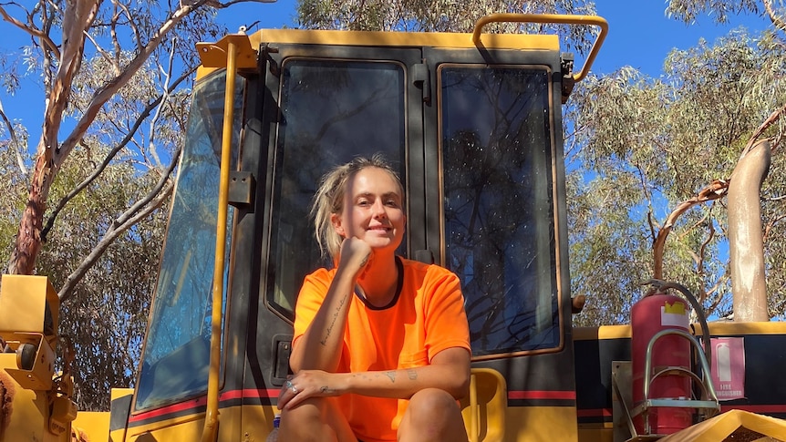 A young woman in a high vis top sitting on a digger.