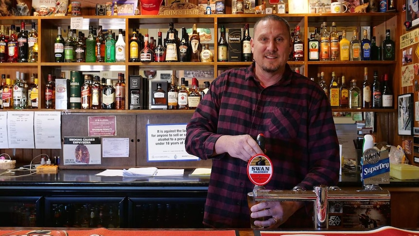Kirk Pohl pours a beer behind the bar in the Perenjori Hotel. Shelves behind him are filled with spirit bottles and bric-a-brac.