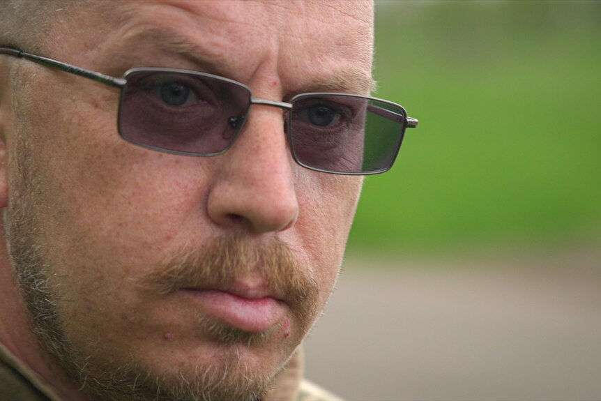 A close up shot of a bald man wearing dark glasses.