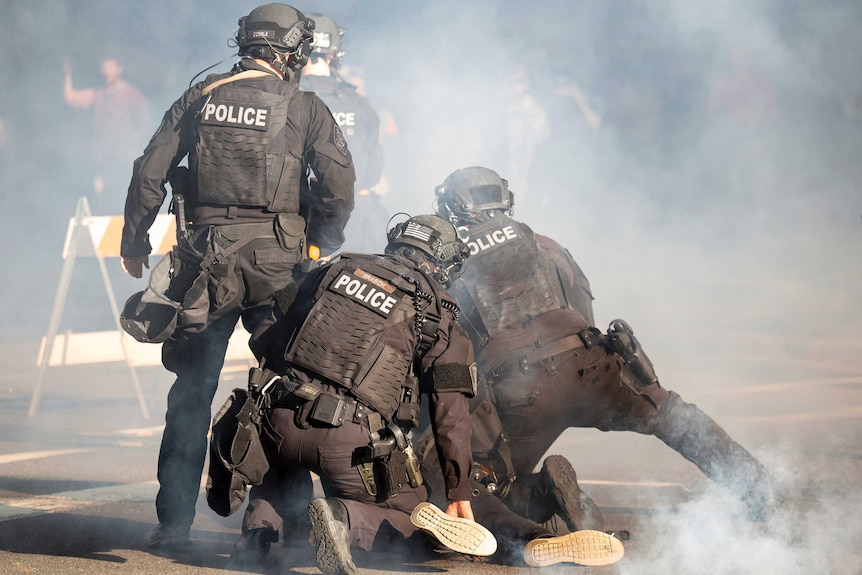 A group of police in a cloud of tear gas surrounding a person on the ground