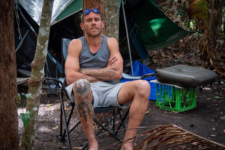 man sitting on camp chair in front of tent wearing singlet