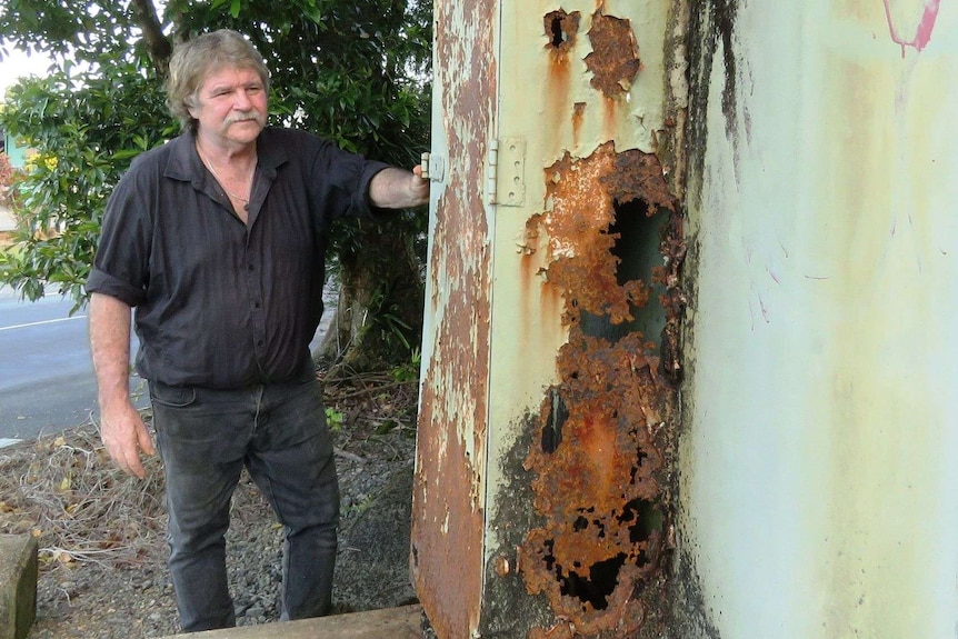 Rodney Edwards standing next to a rusty metal box attached to the molasses tank