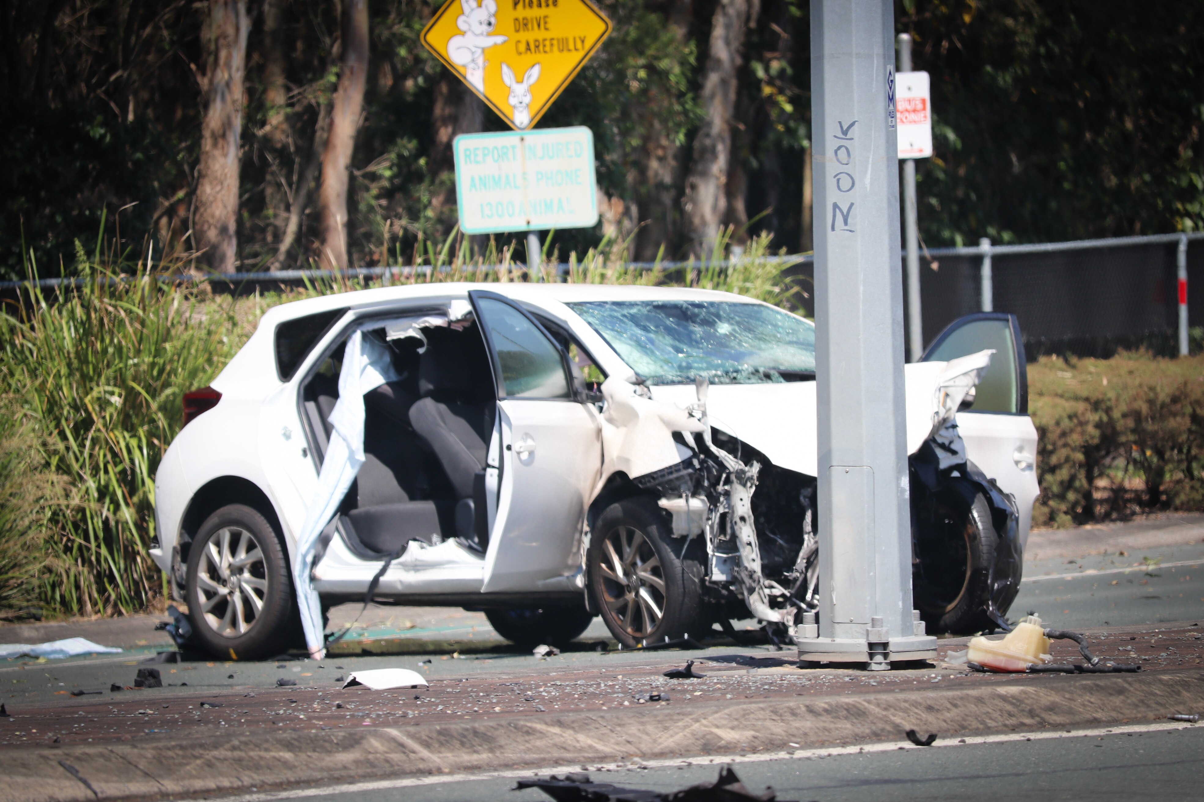A white car with bumper  and side door crumpled rests against a pillar, glass and other debris.