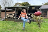 A girl kicking a football in a backyard, while an adult watches on from the verandah.
