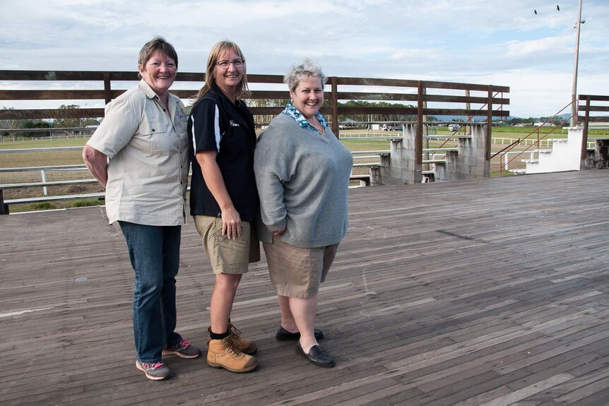 Three women stand in a row on top of a cyclone-destroyed pavilion, the floor of which only survived