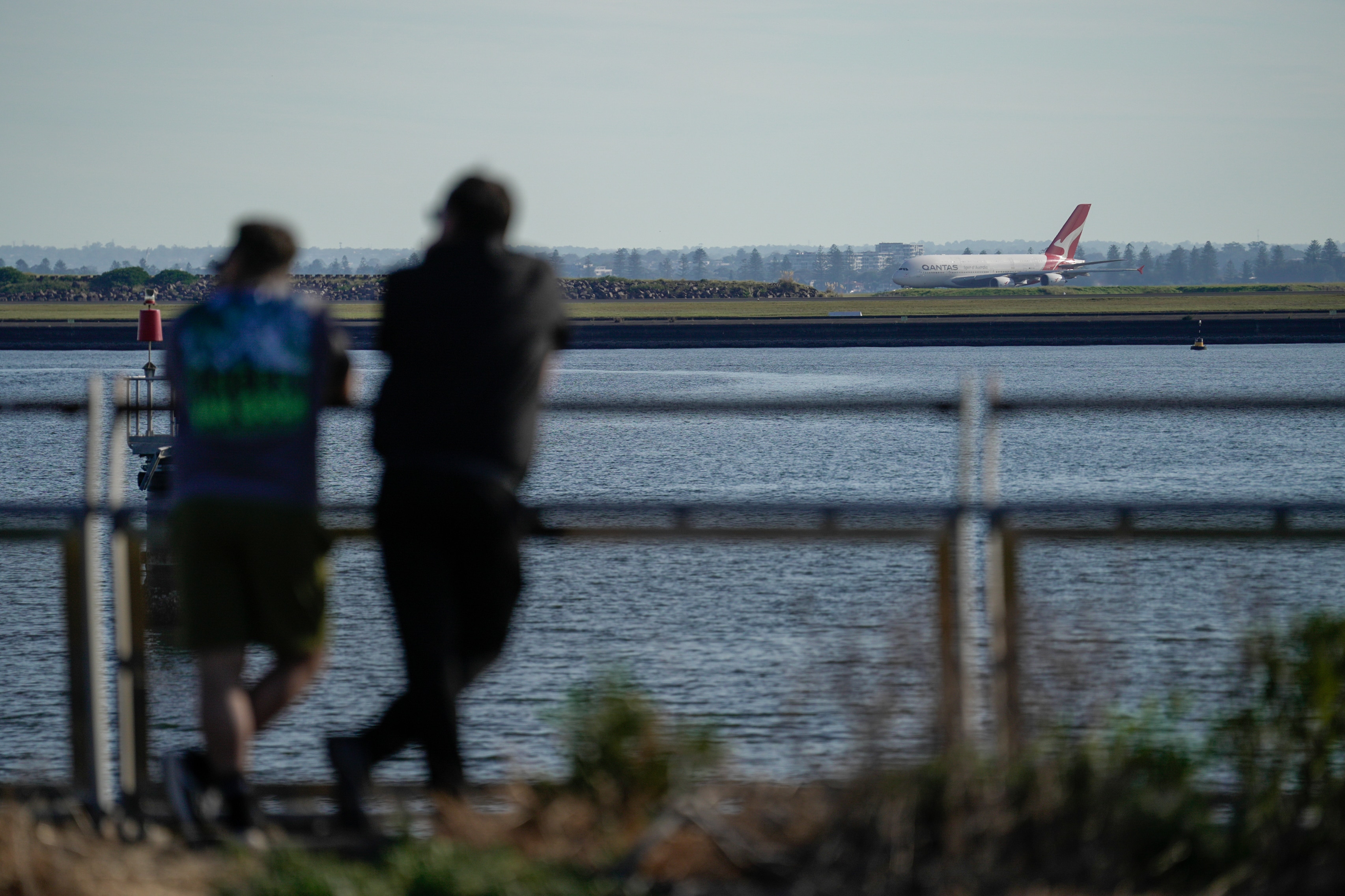 A couple looks across a lake at a Qantas plane on the tarmac