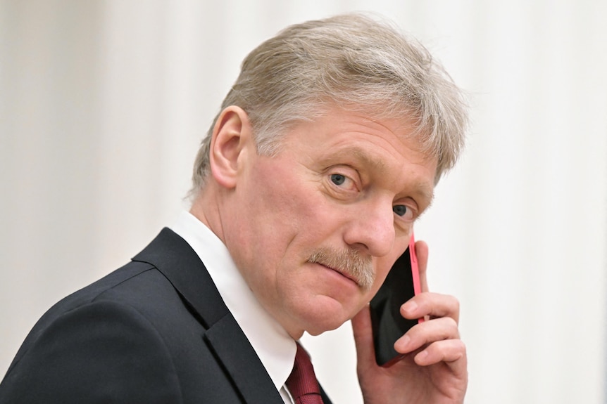 Dmitry Peskov has grey hair and a grey moustache and holds a phone to his ear