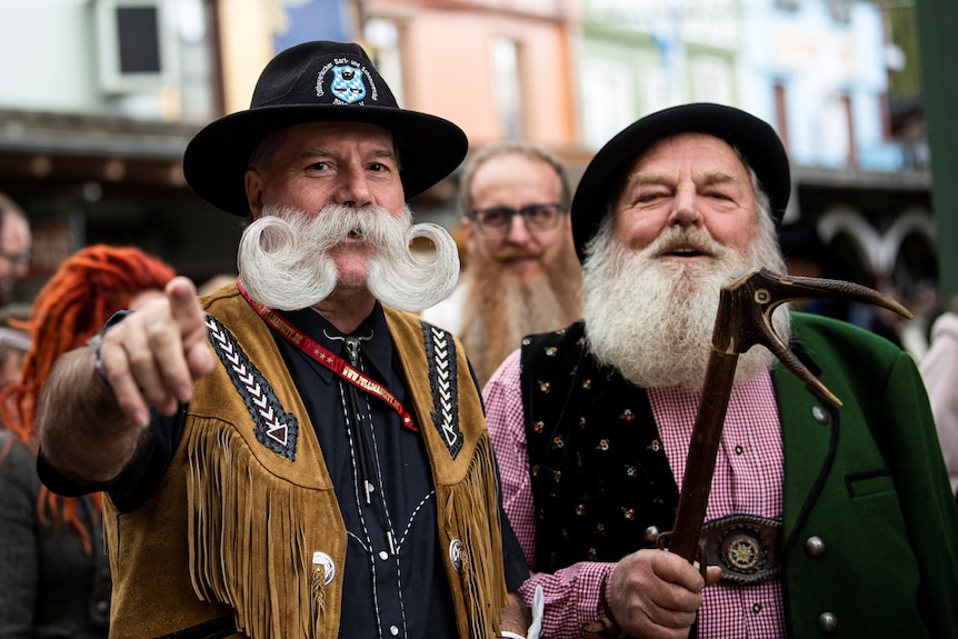 Two older men with a curly white beard and a long straight white beard in a city street 