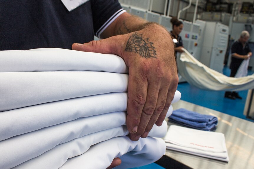 Hands carry folded linen at the Vanguard Laundry