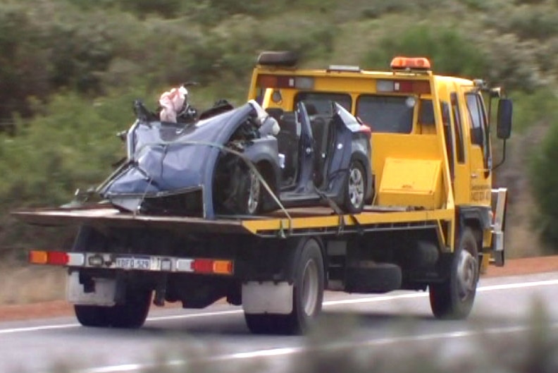 A flat bed truck carrying the wreck of a car involved in a triple fatal head-on collision north of Perth.