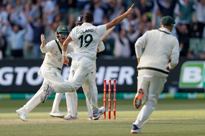 Scott Boland holds his finger up and runs off as the broken stumps stand before him