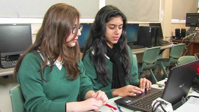 Two teenage girls sit at laptop computer in classroom