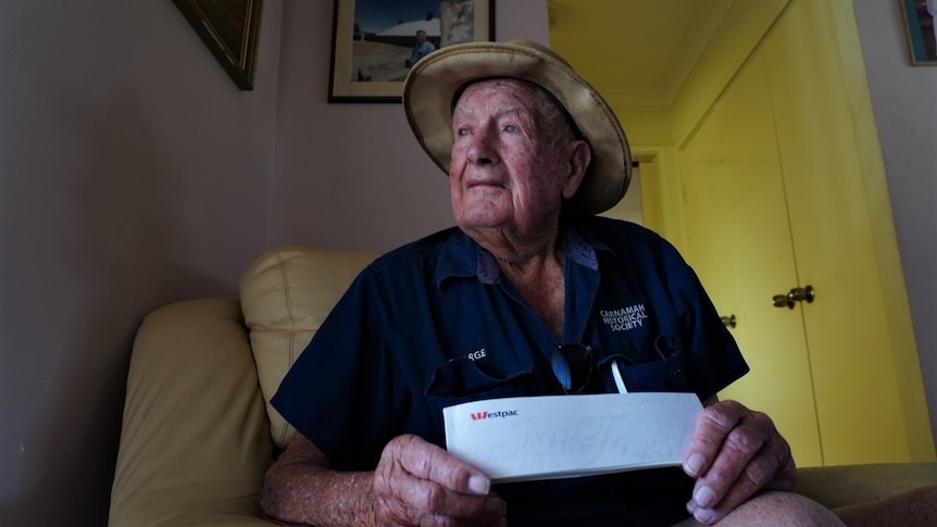 Elderly man sitting in an armchair holding a cheque book.