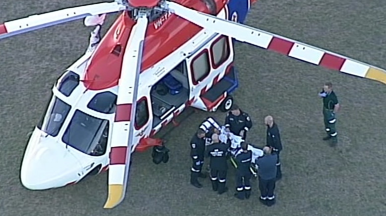 Paramedics load a child on a stretcher into a helicopter in the middle of an oval.