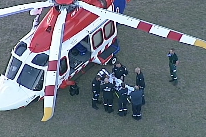 Paramedics load a child on a stretcher into a helicopter in the middle of an oval.