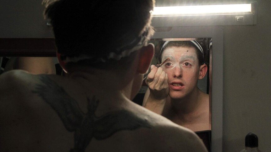 man looking in mirror putting on makeup