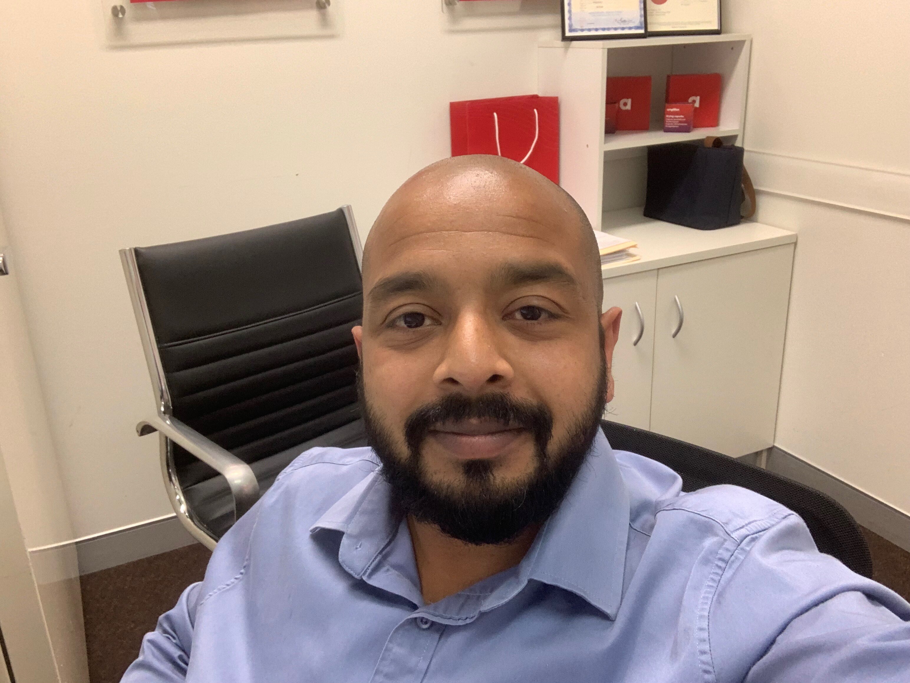A man with facial hair, wearing a blue business shirt, takes a selfie. 