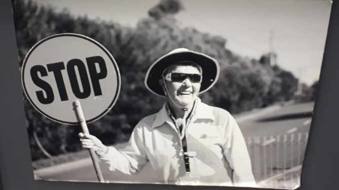 Black and white photo of crossing supervisor carmel black wearing high-visibility jacket, holding a stop sign