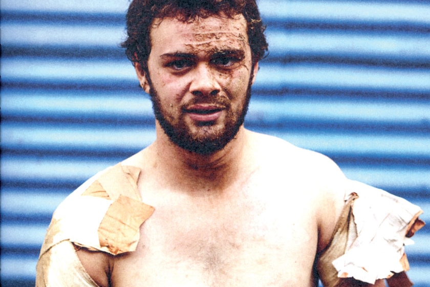 A footballer looks to camera. He is sporting lots of shoulder strapping and has mud and pain all over his face