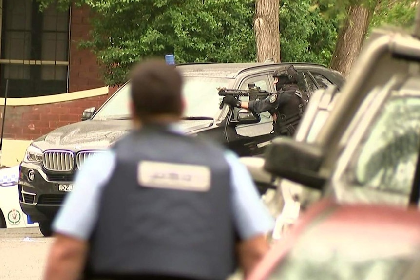 A riot policeman rests a gun on top of a police four wheel drive.