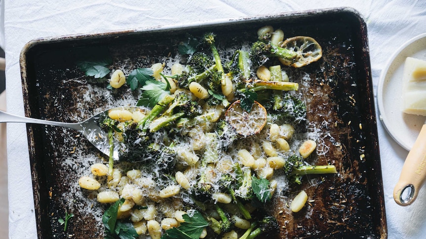 A baking tray with cooked gnocchi, broccoli topped with parsley and cheese, an easy vegetarian dinner recipe from Hetty McKinnon