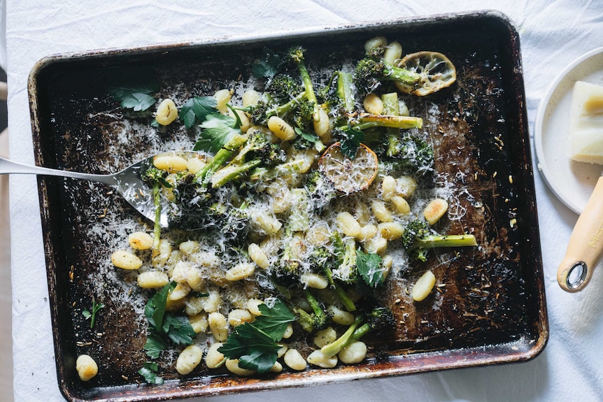 A baking tray with cooked gnocchi, broccoli and lemon topped with parsley and cheese, a fast and easy vegetarian dinner.