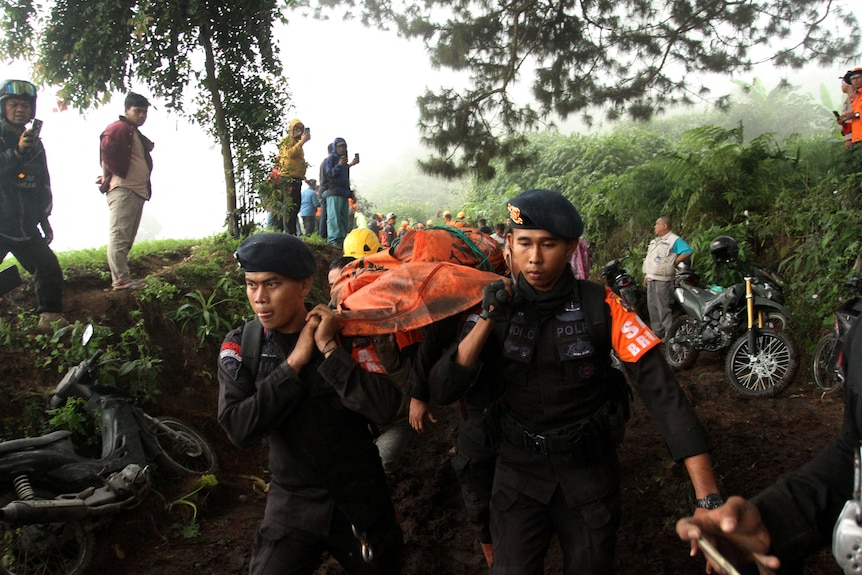 Indonesian police officers carry the body of a Mount Marapi eruption victim.