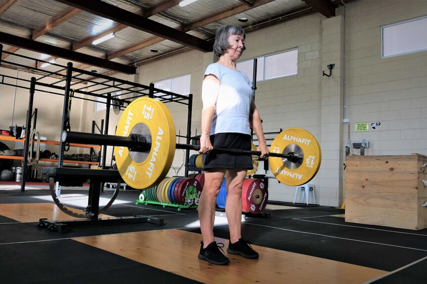 Woman with grey hair deadlifts 50 kilograms in a gym.