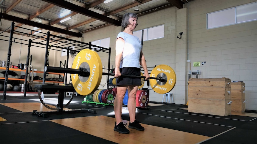 Woman with grey hair deadlifts 50 kilograms in a gym.