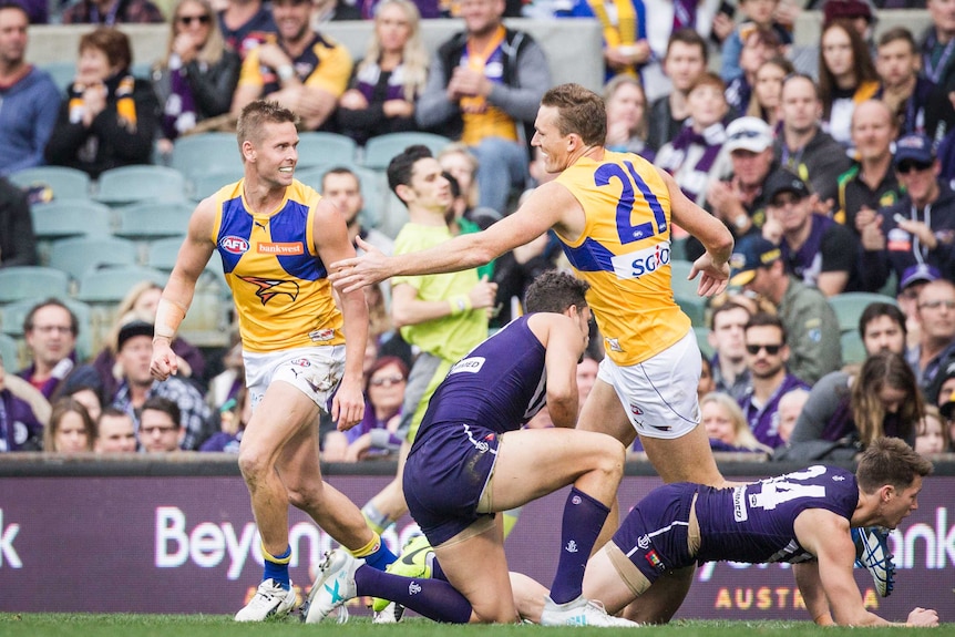 Mark LeCras and Drew Petrie celebrate a goal for the West Coast Eagles with two Fremantle Dockers players on the ground.