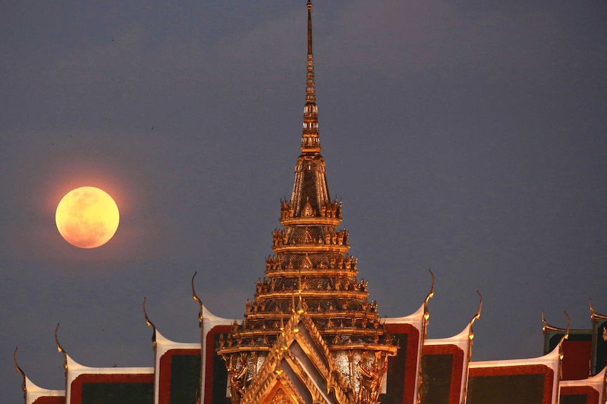 A full moon rises beside the Grand Palace in Bangkok, Thailand.