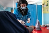 A woman in scrubs and a headscarf checking the blood pressure of someone in a medical room