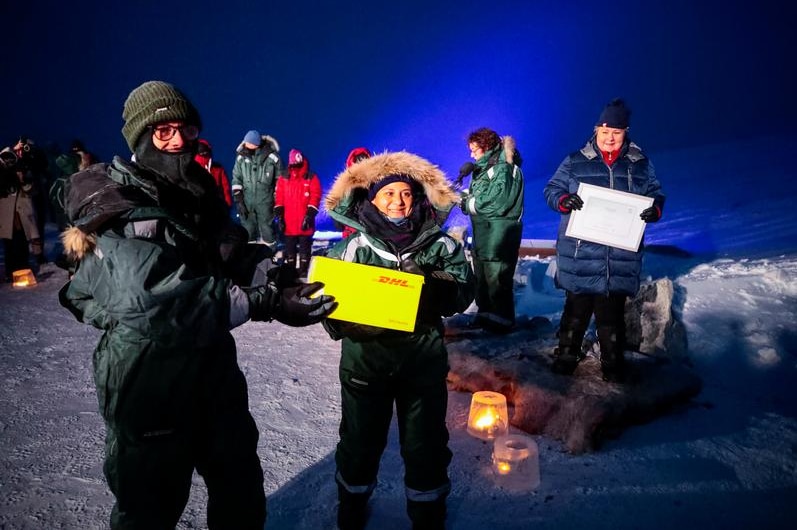 People  holding up a yellow parcel near the arctic vault.