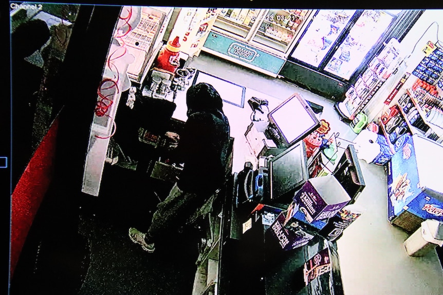 two hooded youths standing behind a petrol station counter breaking into a cupboard