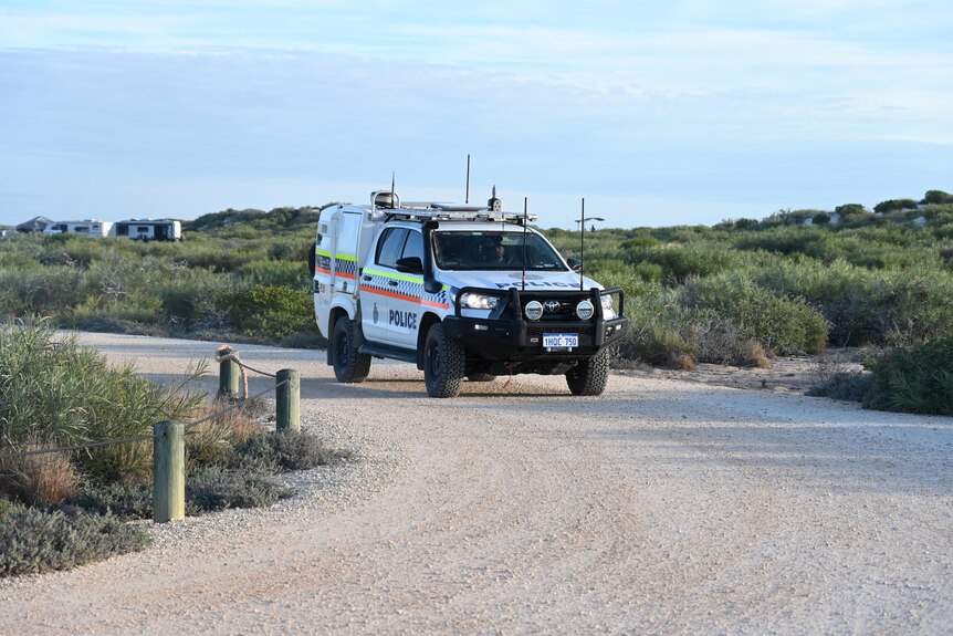 A police vehicle parked on a sandy track. 