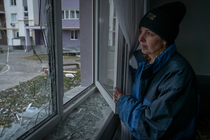 A woman wearing a black headbank and blue jumper stares out the window.